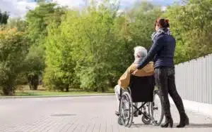 badante che spinge anziano in sedia a rotelle