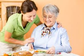 Badante che aiuta una anziana a cui ha appena preparato il pranzo a mangiare